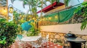 An outdoor patio with a stone wall, a table with chairs, string lights, and a grill. - Playacar Paradise | Pool | Patio | Steps to Beach (Playa del Carmen)