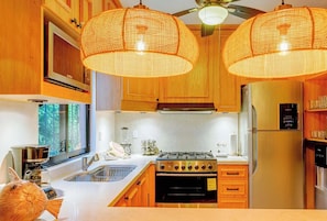 Une cuisine moderne avec des meubles en bois, un réfrigérateur en acier inoxydable, une cuisinière à gaz et des luminaires suspendus.