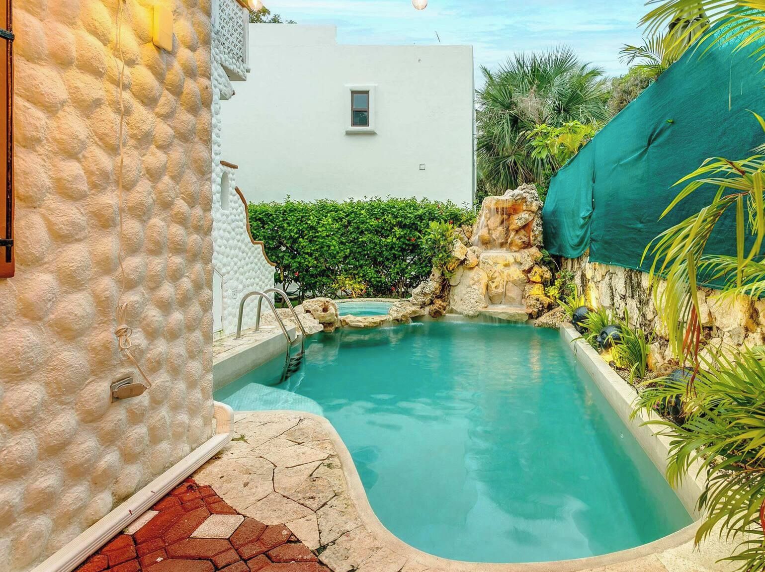 A swimming pool with a waterfall feature, surrounded by a stone wall and greenery.
