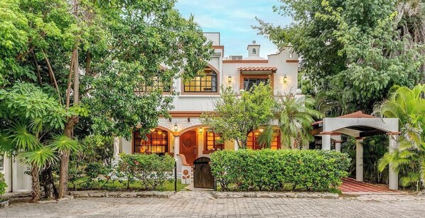 A two-story building with a garden entrance, a covered porch, and a small tower-like structure. - 6BR villa w/ pool, BBQ & backyard (Playa del Carmen)
