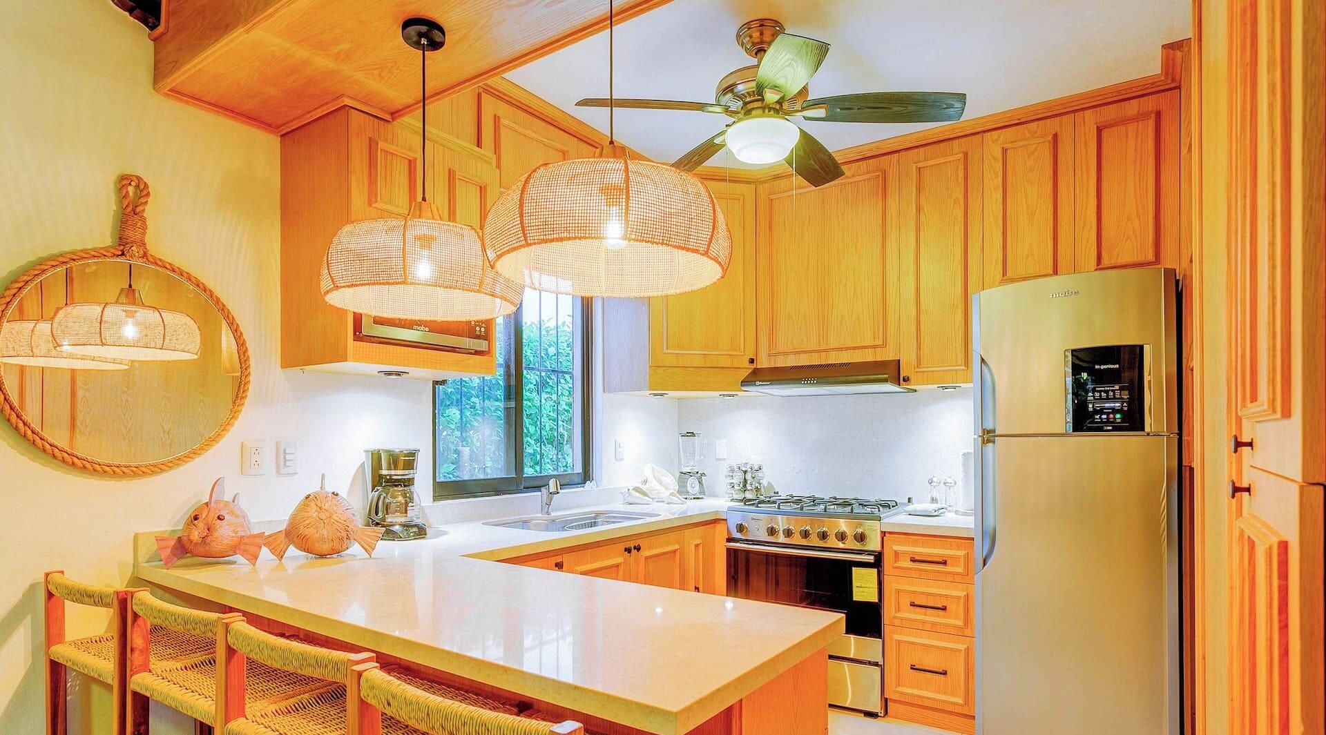 Une cuisine avec des meubles en bois, un îlot central, une cuisinière, un réfrigérateur et des luminaires suspendus.
