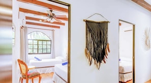 Ein Zimmer mit einem Bett, einem Sessel, einem Deckenventilator, einem Fenster und einer Wanddekoration.
