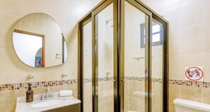 A bathroom with a round mirror, a sink, a toilet, and a shower enclosure. - Playacar Paradise | Pool | Patio | Steps to Beach (Playa del Carmen)