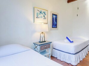 Une chambre avec deux lits, une table de chevet avec une lampe et deux tableaux accrochés au mur.