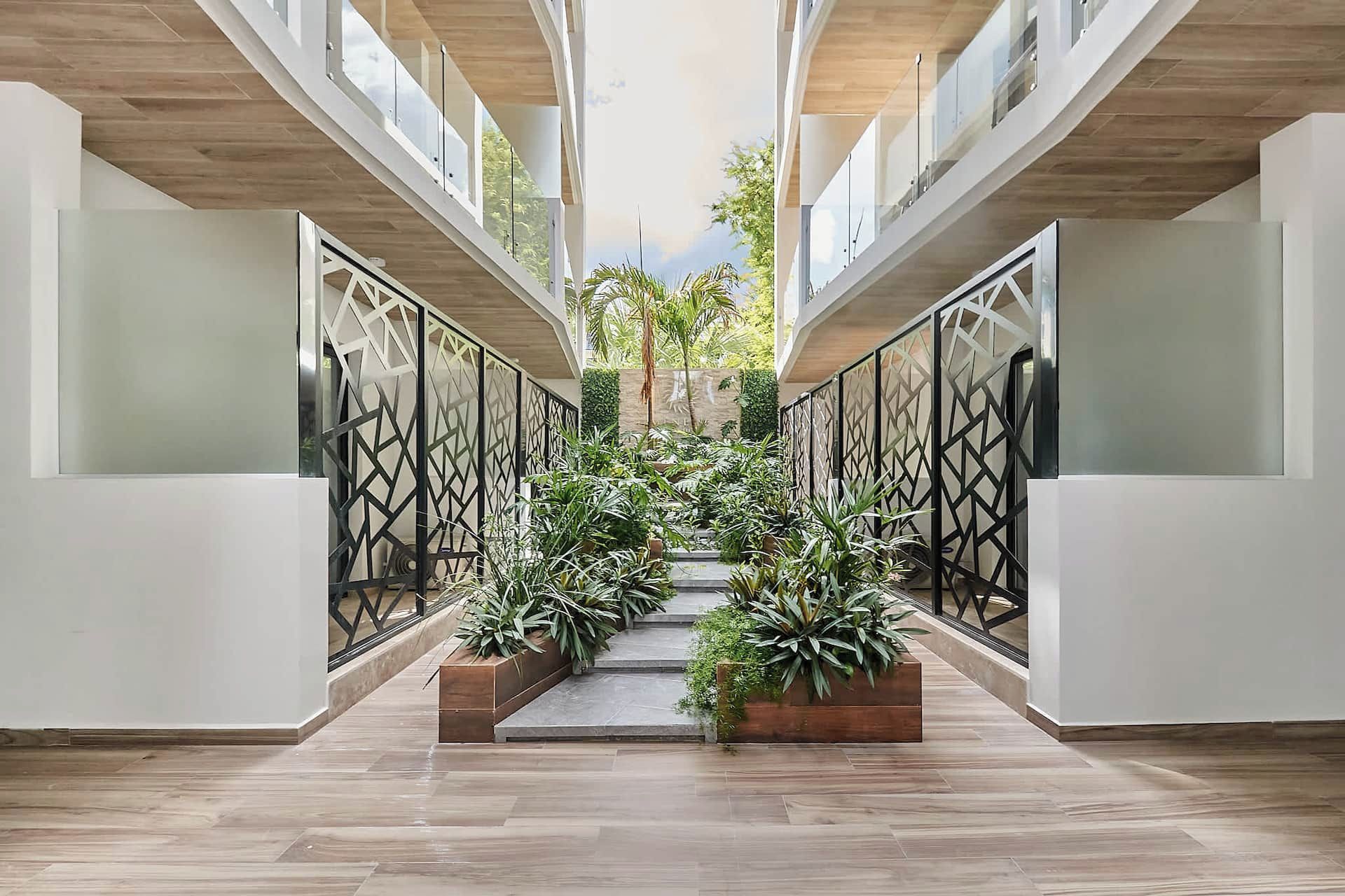 A modern interior with a central staircase flanked by geometric metal railings, leading to a balcony area with plants.