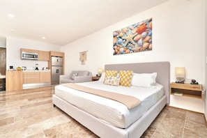 A modern hotel room with a large bed, a kitchenette, and a decorative wall art piece. - Coastal escape w/ rooftop pool, gym & beach walk (Playa del Carmen)