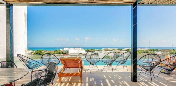 A terrace with a view of the sea, outdoor seating, and a pool. - Oceanview Pool | Gym | 5th Ave Around the Corner (Playa del Carmen)