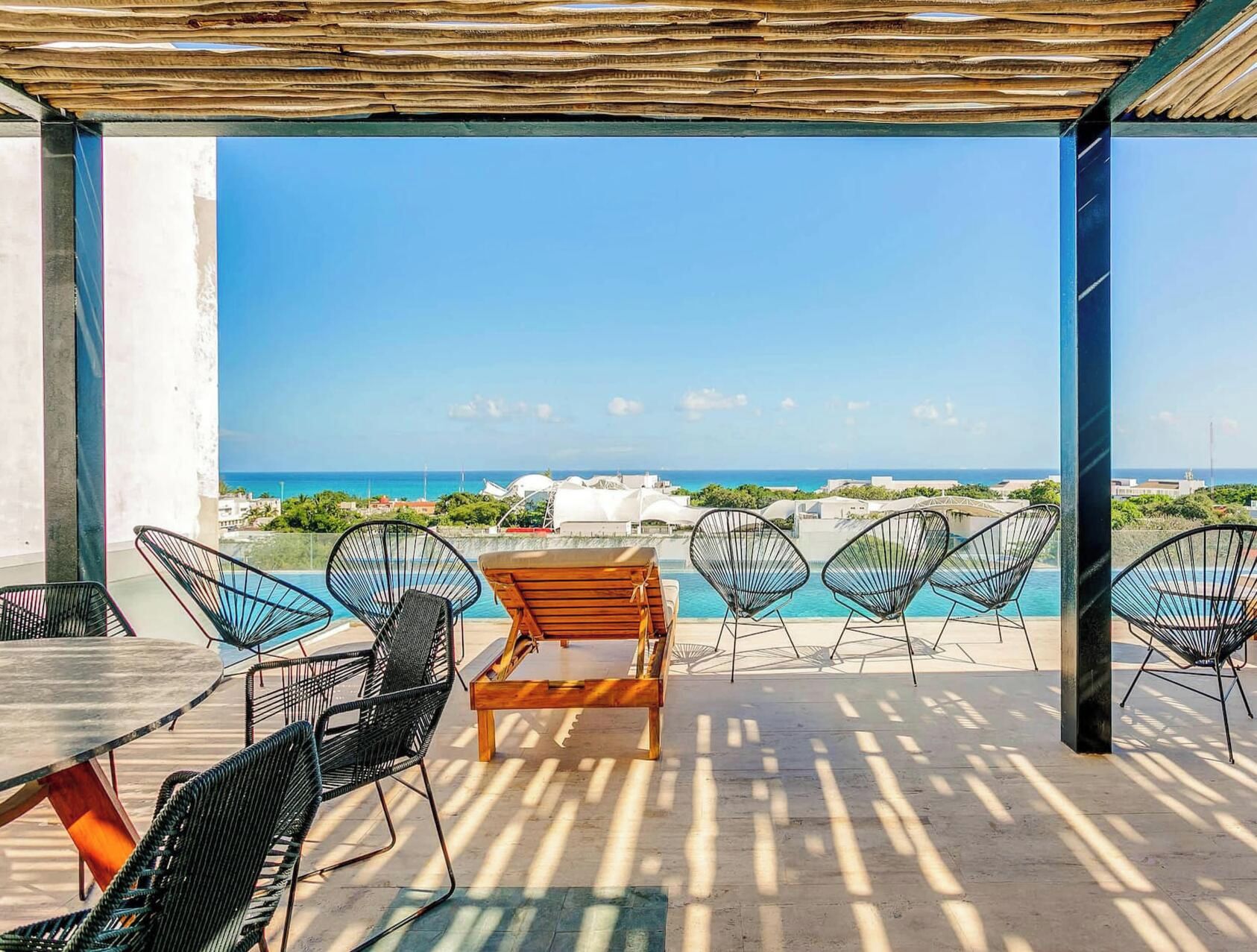 Un espace extérieur aménagé avec des sièges, offrant une vue sur la mer, comprenant une table et des chaises en bois, et une piscine en arrière-plan.