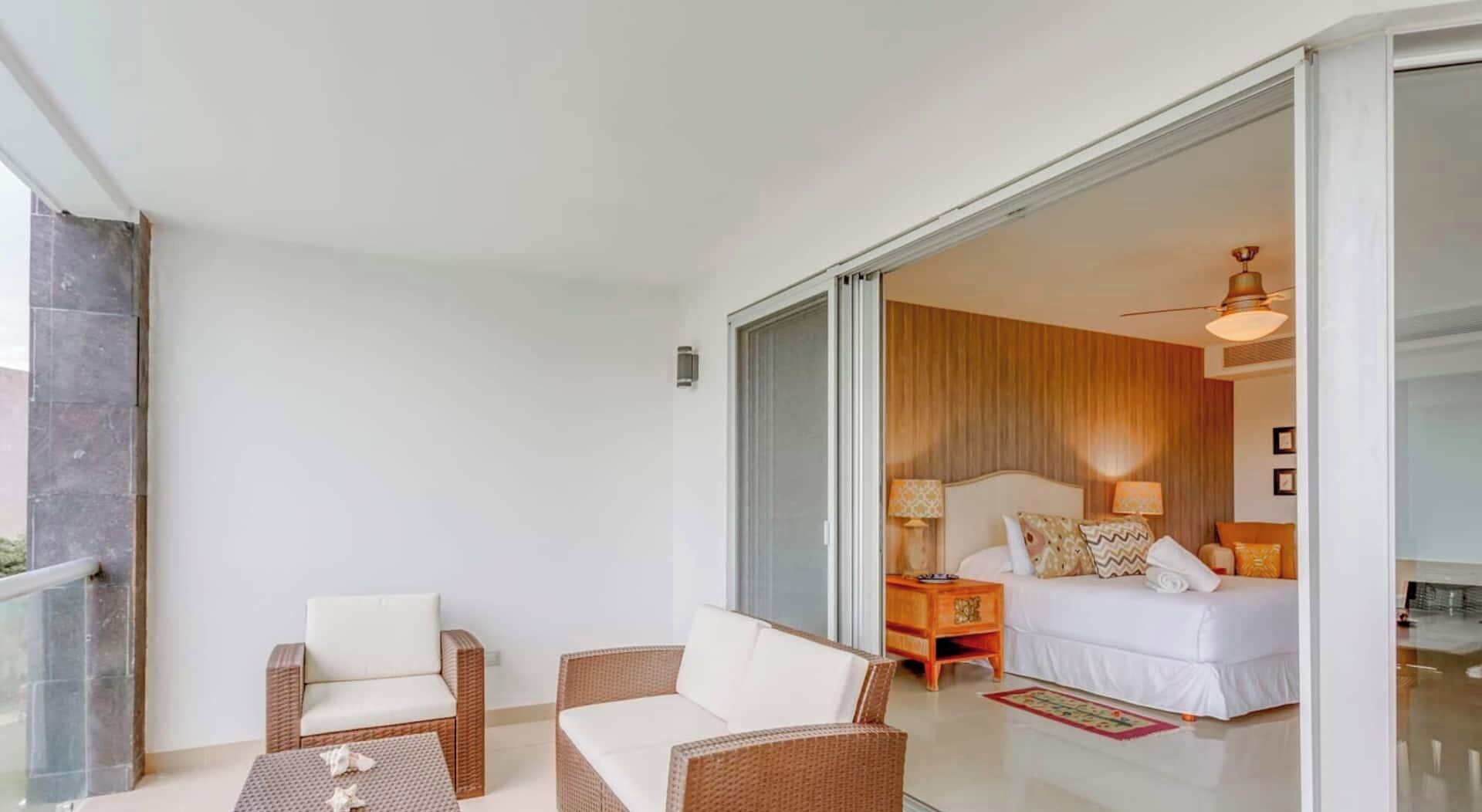 Habitación de hotel con cama, dos sillas, una mesa y puerta corrediza de vidrio que da a un balcón.