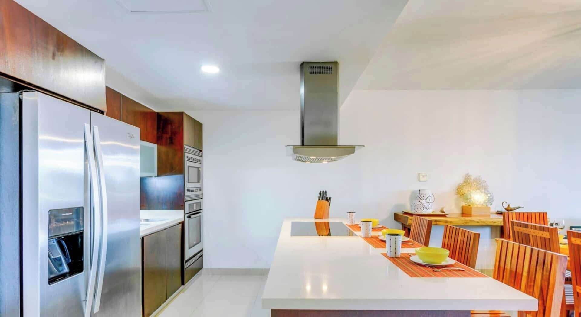 Une cuisine moderne dotée d’appareils électroménagers en acier inoxydable, d’un îlot central et d’un coin repas avec des chaises en bois.