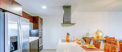 Une cuisine moderne dotée d’appareils électroménagers en acier inoxydable, d’un îlot central et d’un coin repas avec des chaises en bois.