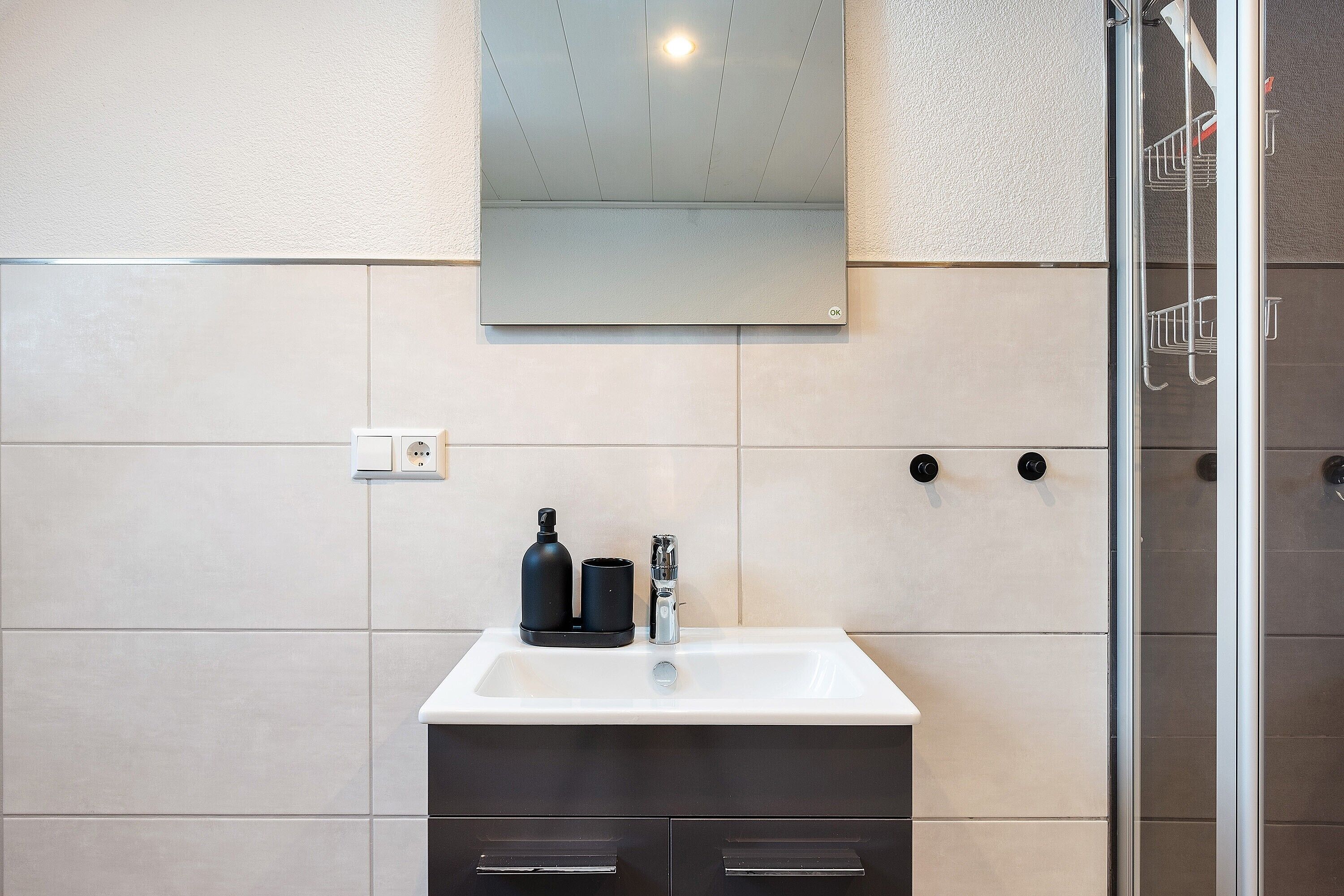 Une salle de bain avec un lavabo blanc, des meubles sombres, un miroir et une cabine de douche en verre.