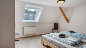 Una camera da letto con soffitto spiovente, una finestra a lucernario, un letto con copriletto decorato, una sedia e un termosifone.