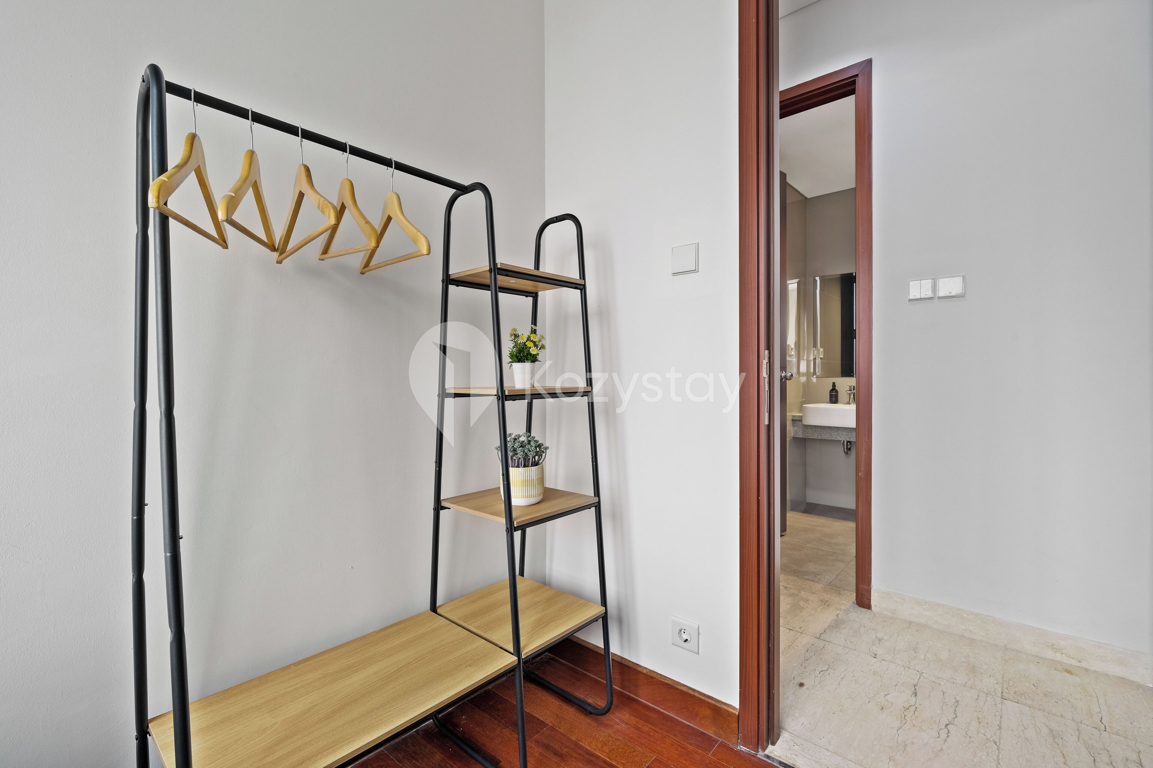 A room with a metal shelf unit against the wall, a wooden bench, and a door leading to a bathroom.