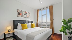 A modern hotel room with a large bed, a nightstand with a lamp, a window with curtains, and a view of the city. - Anlan by Kozystay - Taman Sari (Jakarta)