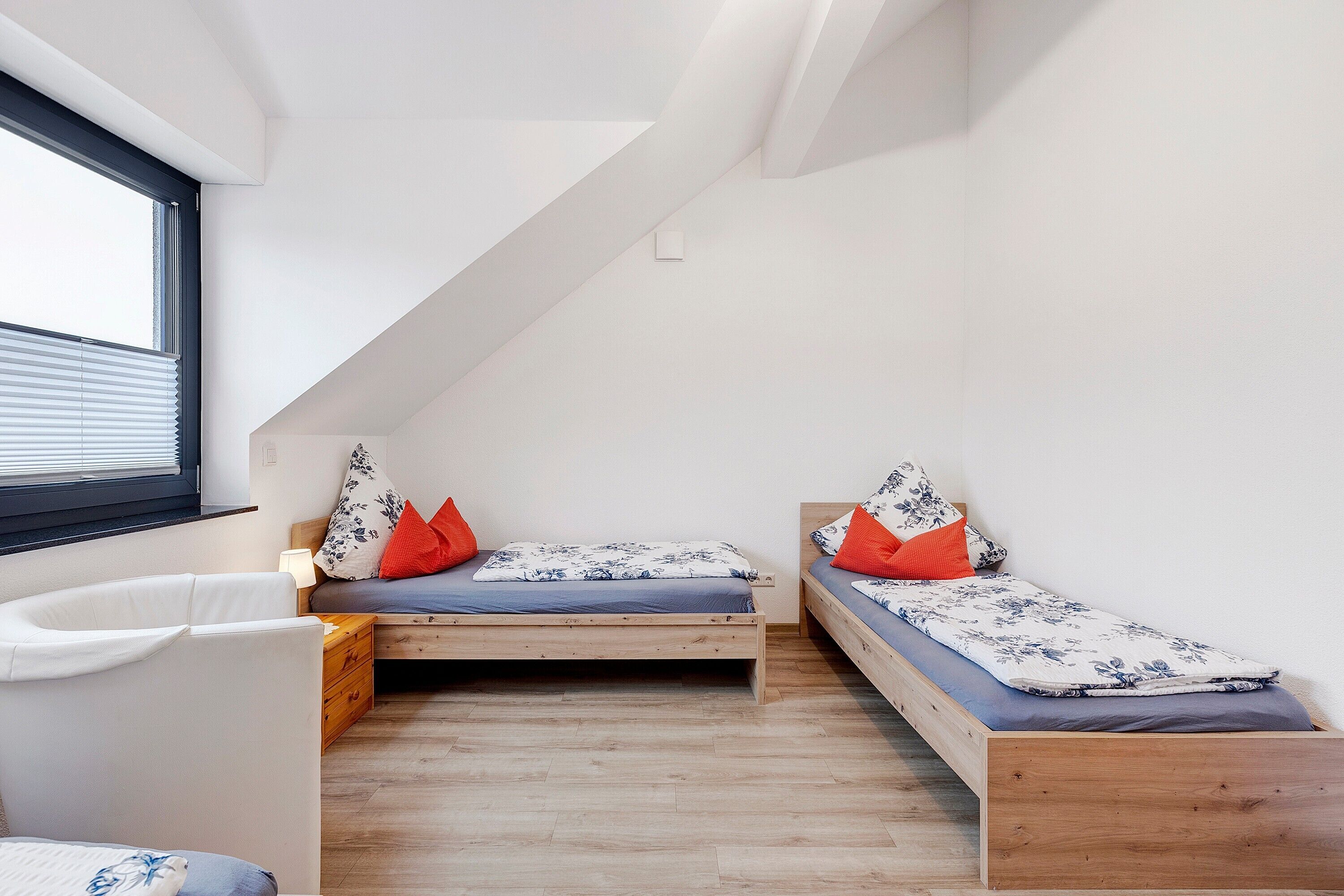 Ein kleiner, moderner Raum mit zwei Holzbett und einem weißen Stuhl, sowie einem Fenster.