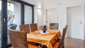 A dining area with a table set for four, surrounded by wicker chairs, a vase with flowers, and a view through a glass door. - Deluxe Apartment Lea with Balcony and Wi-Fi (Radolfzell am Bodensee)