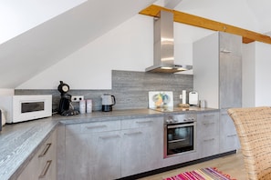 Una cucina moderna con forno a microonde, macchina del caffè e tostapane integrati, un grande forno e una trave a vista in legno.