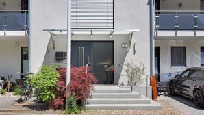 Ein modernes Gebäude mit einer Wendeltreppe, einem geparkten Auto vor der Fassade und einem Tisch mit Topfpflanze im Erdgeschoss.