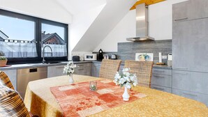 Eine moderne Küche mit Essbereich, Blick durch ein Fenster und einer hohen Decke mit freiliegenden Balken.