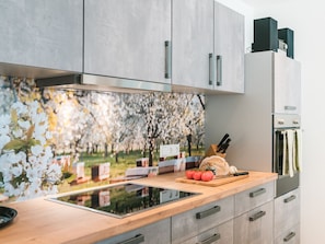 A modern kitchen with a built-in induction cooktop, wooden countertop, and grey cabinetry. - Apartment "12 Kirschen" with Shared Terrace, Garden and Wi-Fi (Durbach)