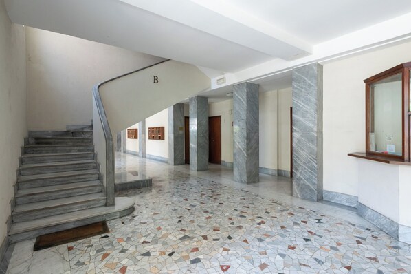 Um hall amplo com escadaria de mármore, piso ladrilhado e balcão de recepção.