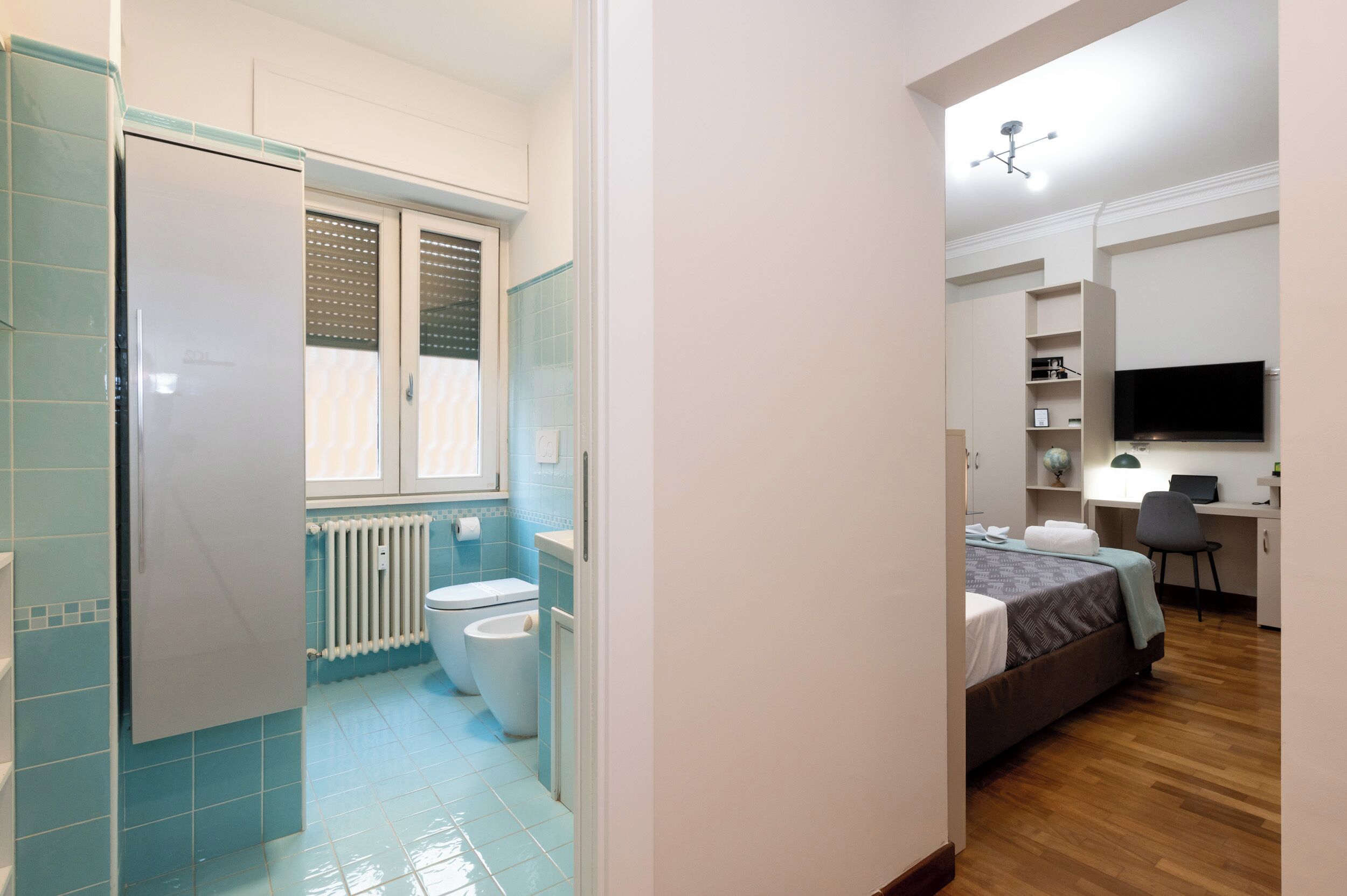 Ein gemütlicher Raum mit Bett, Schreibtisch, Fernseher und einem Badezimmer mit Toilette und Heizkörper.