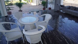 A modern indoor patio with a glass-top table surrounded by wicker chairs, a sofa, and potted plants. - Shree Jagannath Resort (Shri Madhopur)
