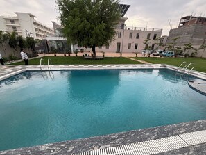 A swimming pool with a checkered border, surrounded by a well-maintained lawn and a building with multiple windows. - Shree Jagannath Resort (Shri Madhopur)
