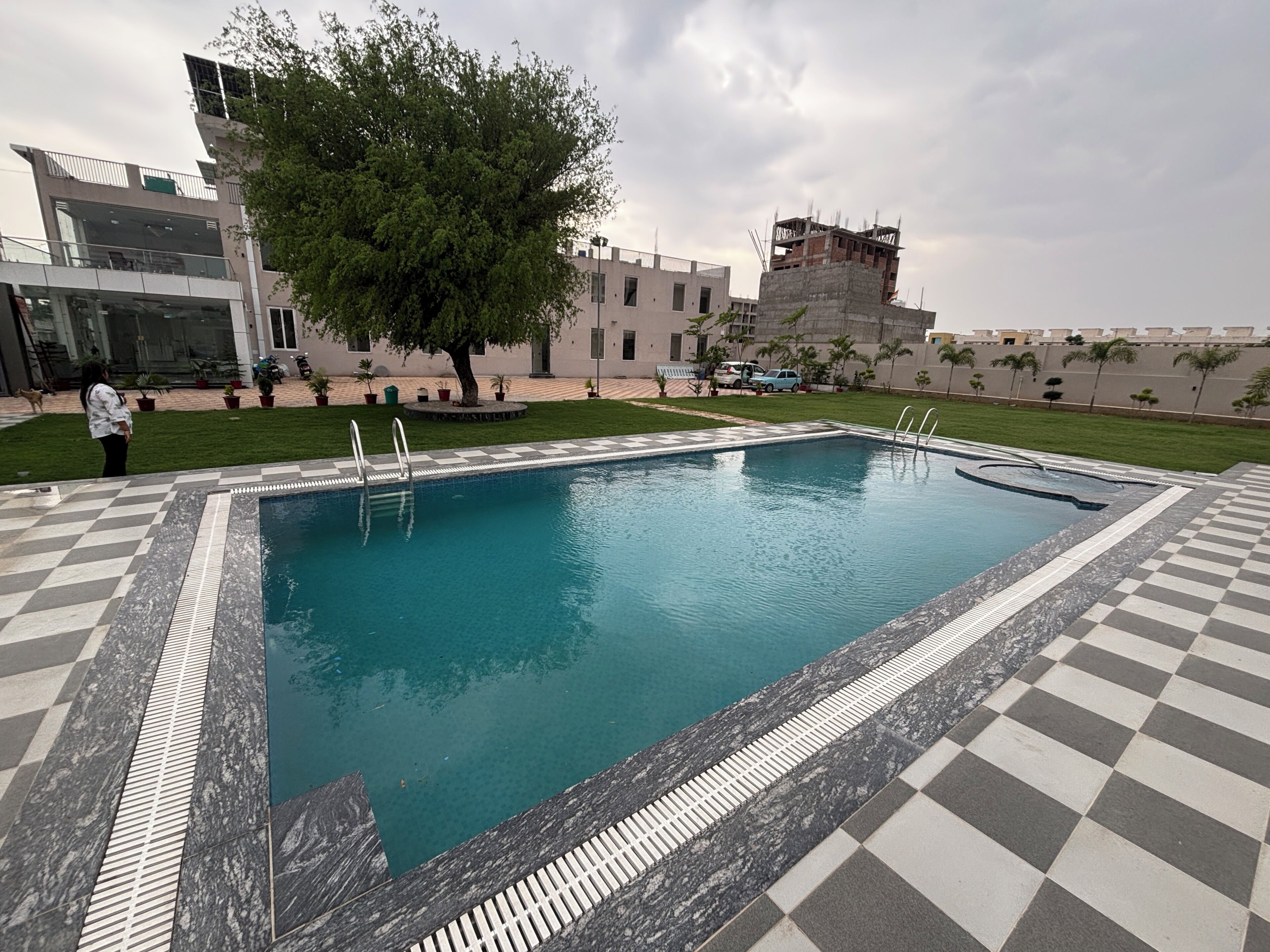Una piscina con baldosas a cuadros, un árbol y un edificio al fondo.
