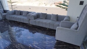 A modern living room with a grey sofa set, a glossy black marble floor, and a view of a landscaped area outside. - Shree Jagannath Resort (Shri Madhopur)