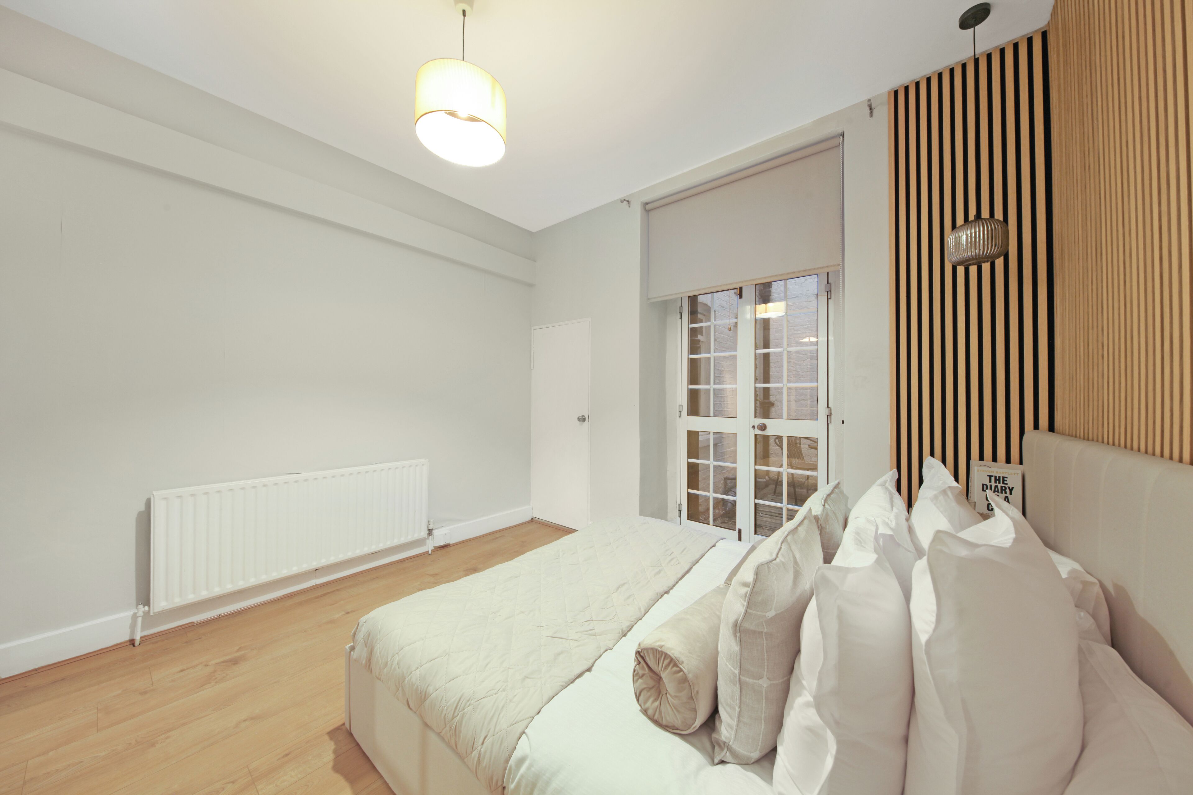 A bedroom with a bed, a radiator, a window with blinds, and a wooden panel wall.