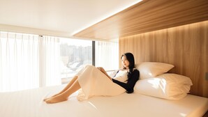 A modern hotel room with a large bed, a wooden headboard, and a view of the city through the window. - Loft13 Hostel (Seoul)