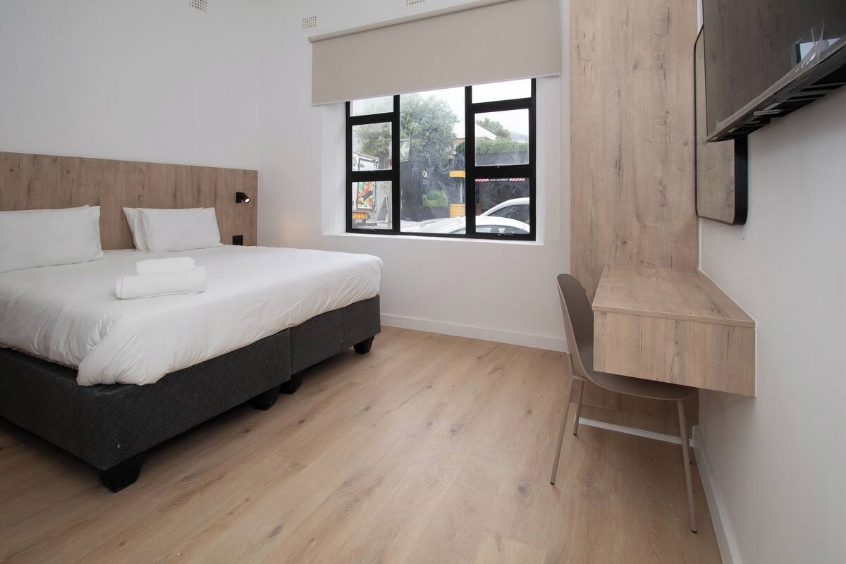 Ein modernes Schlafzimmer mit Bett, Schreibtisch und einem Fenster mit Blick ins Freie.