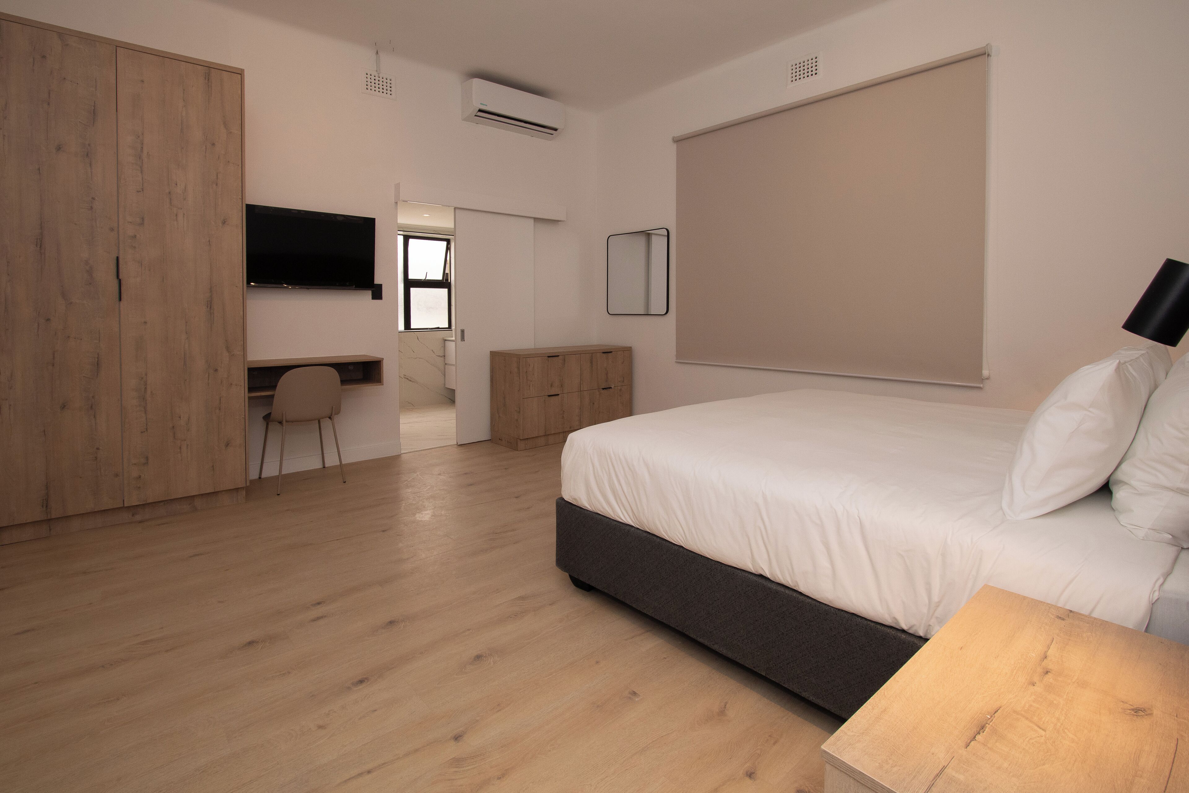 A modern bedroom with a large bed, a desk, and a wardrobe.