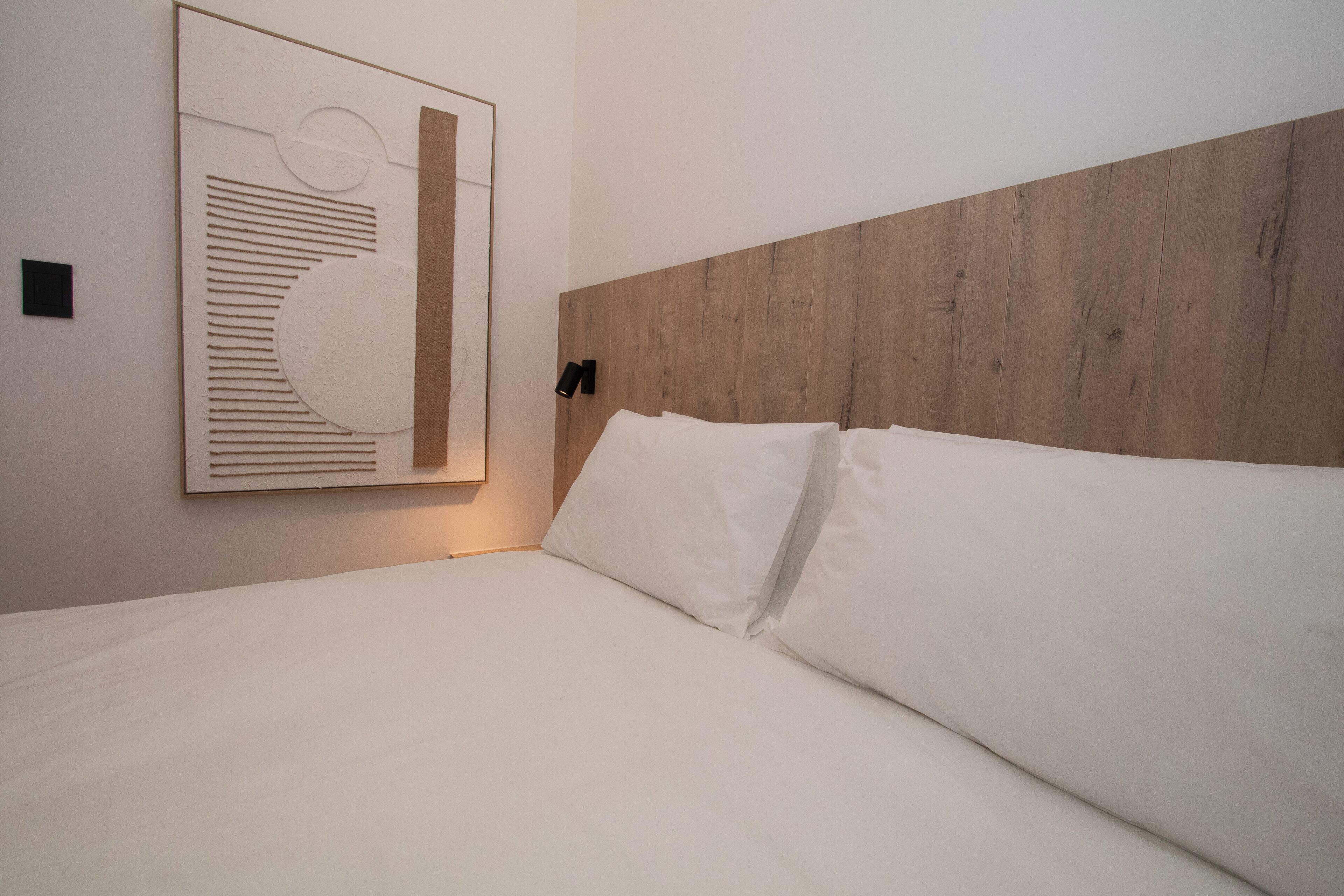 Een moderne hotelkamer met een houten hoofdeinde, wit beddengoed en een groot abstract kunstwerk aan de muur.
