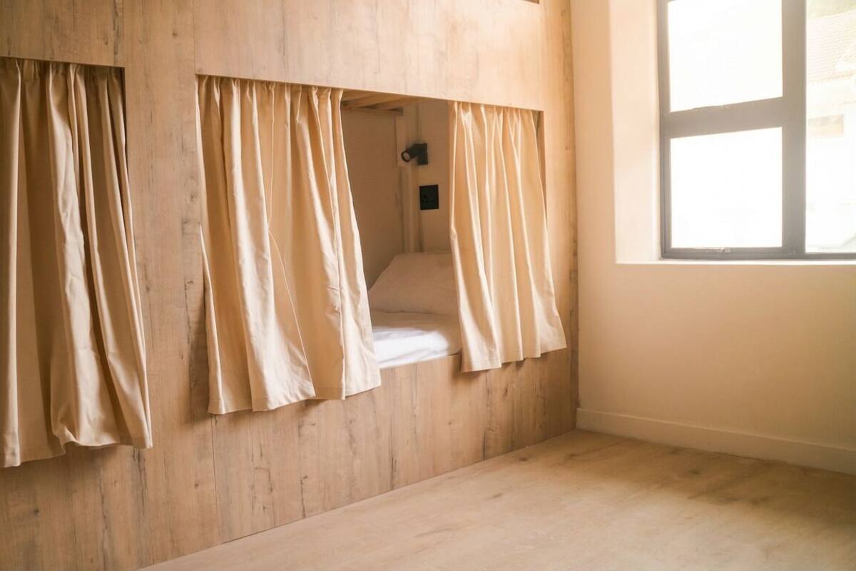 Ein Zimmer mit Holzboden und -wänden, einem Fenster und einem Bett mit Vorhängen.