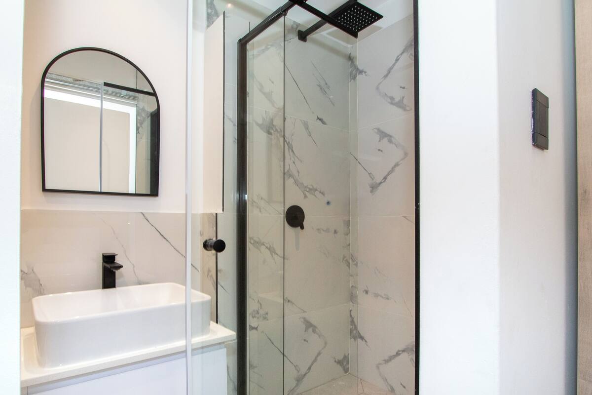 Ein modernes Badezimmer mit einer Glaskabine zur Dusche, einem weißen Waschbecken und einer Marmor-Spritzschutzwand.
