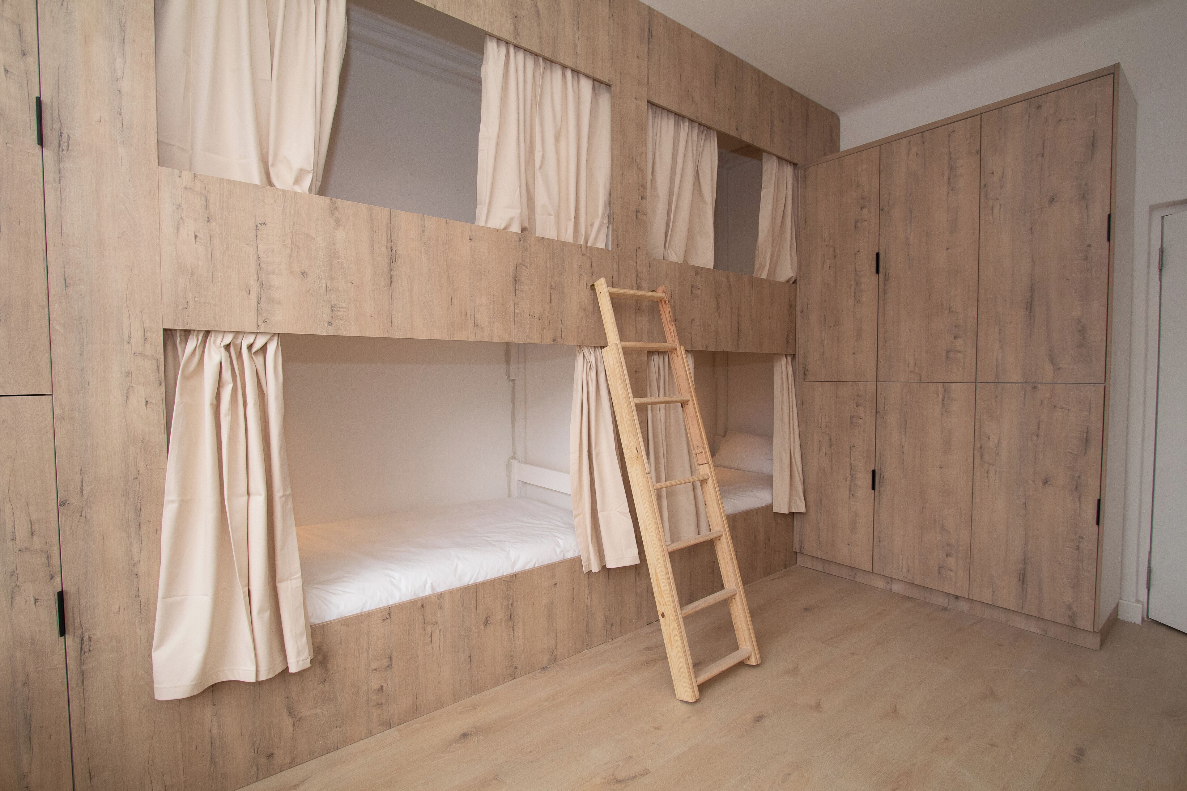 A bunk bed room with wooden walls, a ladder, and curtains.