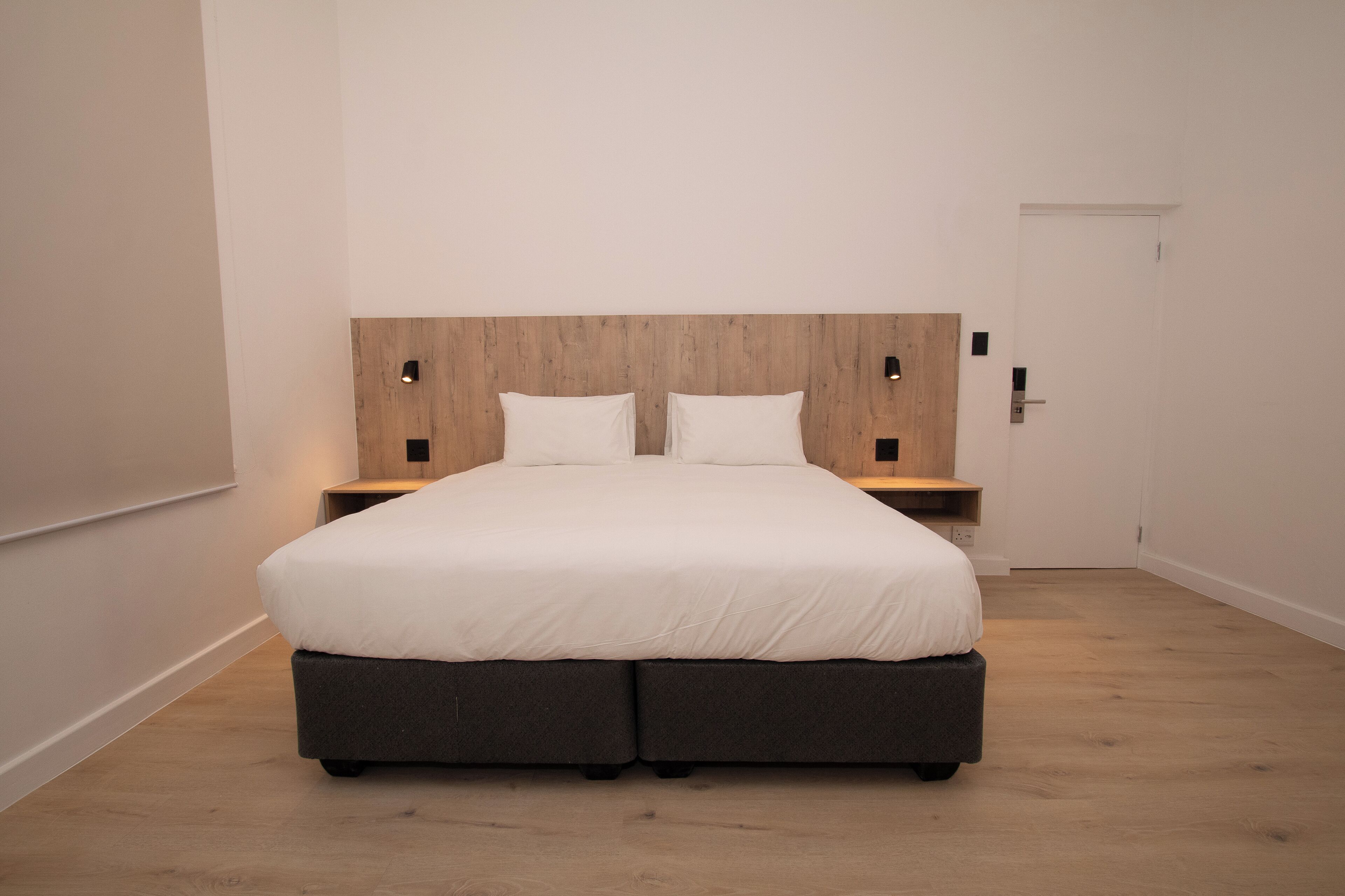 A modern bedroom with a large bed, wooden headboard, bedside tables, and a door.