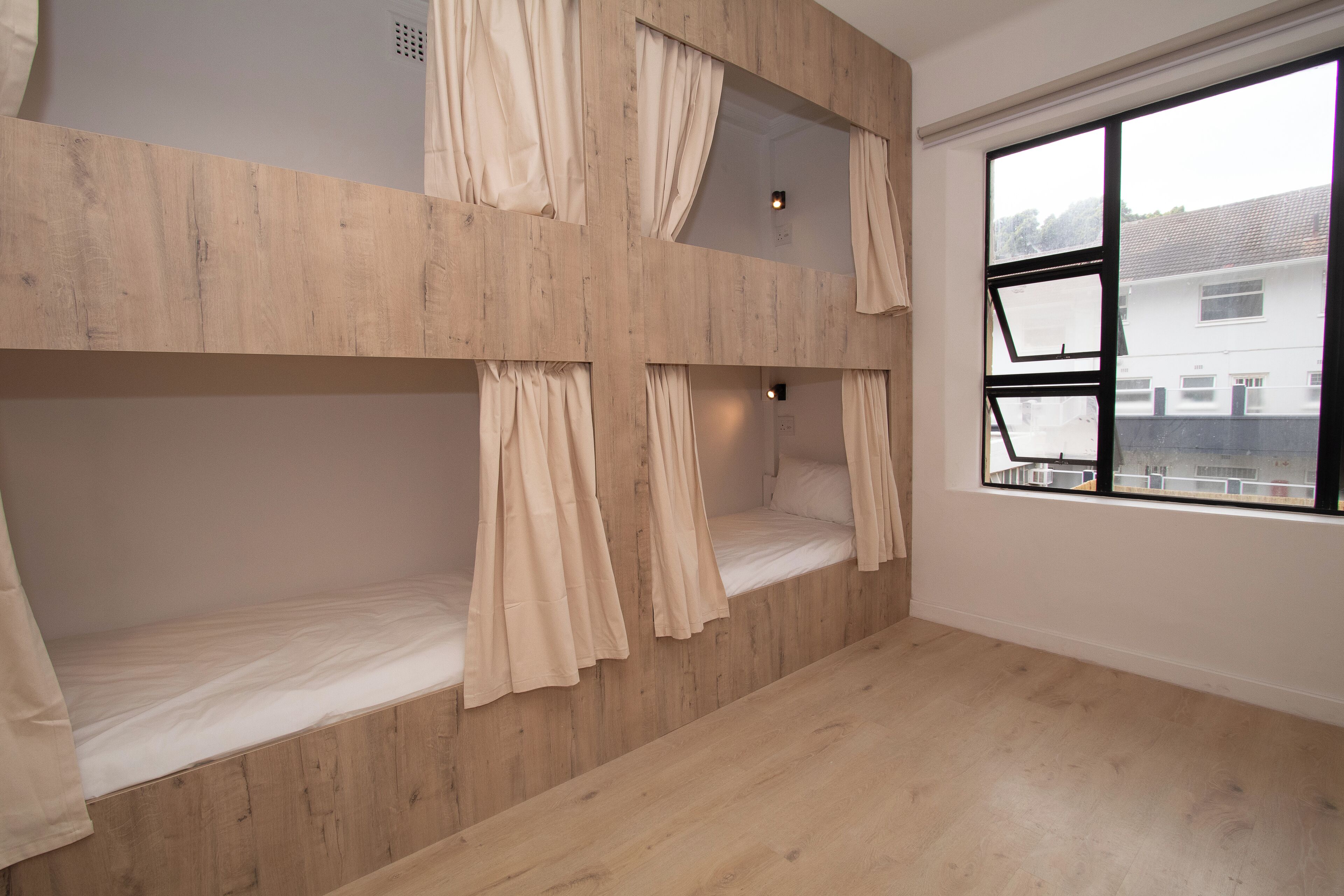 Una habitación con literas, paredes de madera, un ventanal y vistas a edificios.
