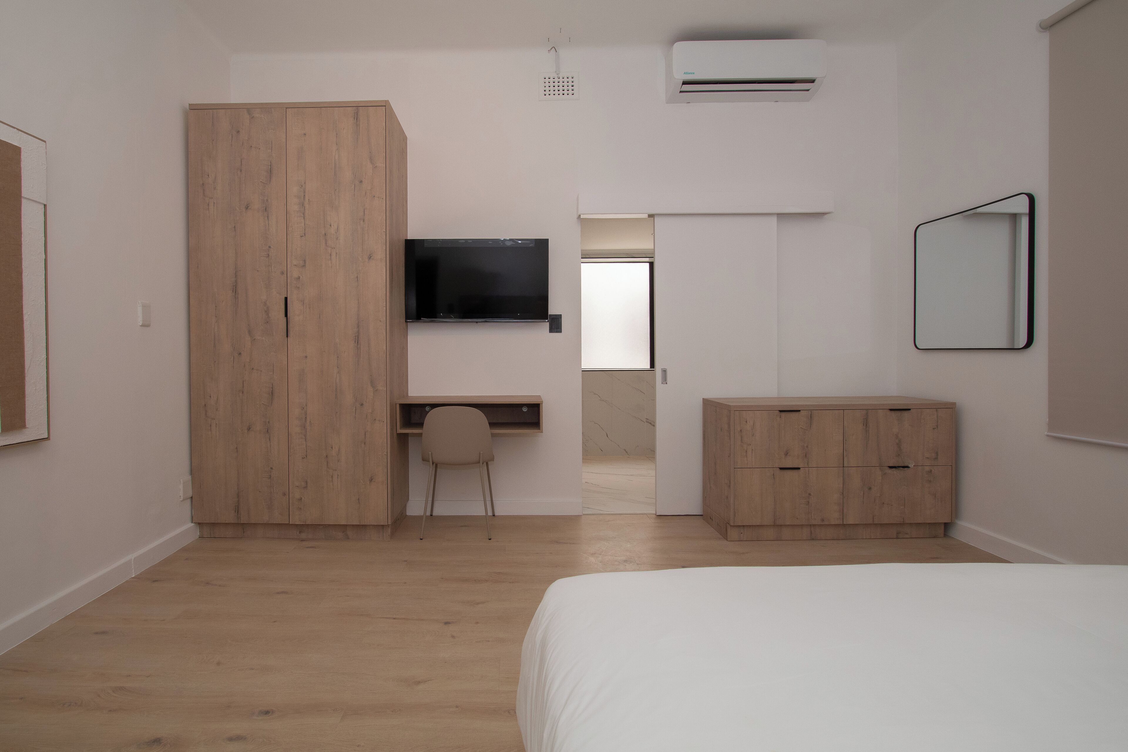 Une chambre à coucher comprenant un lit, une armoire en bois, un bureau avec une chaise, une télévision et une commode.