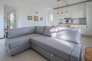 Un soggiorno moderno con un divano modulare grigio, una cucina con mobili bianchi e una zona pranzo.