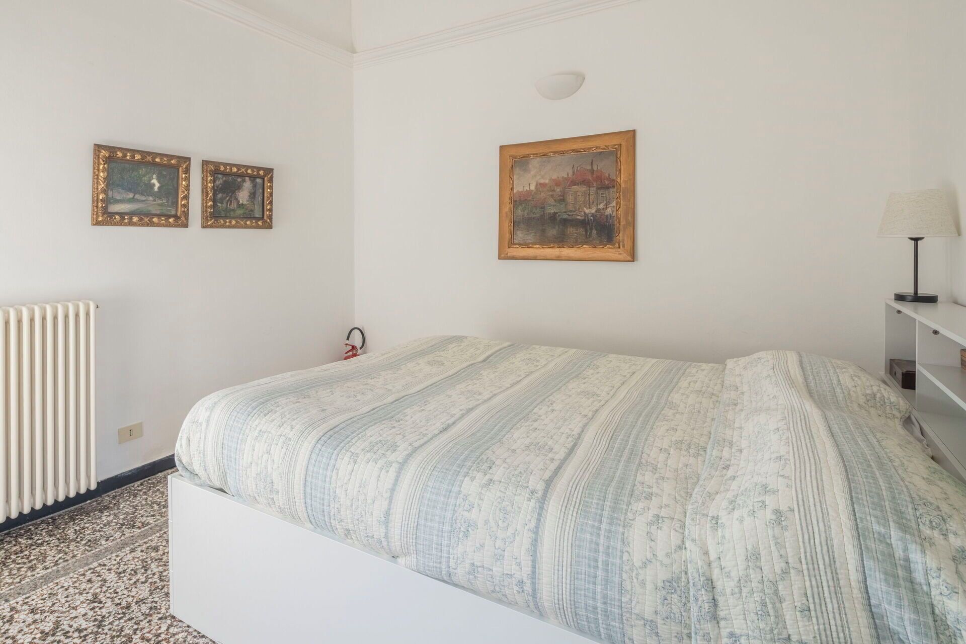 A bedroom with a bed, a radiator, and three framed pictures on the wall.