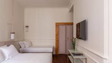 A hotel room with two beds, a desk with a flat-screen TV, a vase with flowers, and a wooden door.