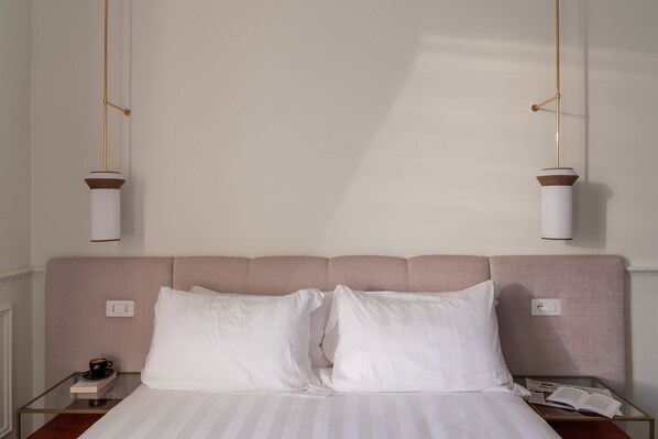 A neatly made bed with white linens and two pillows, a bedside table with a book and a cup, and a wall-mounted light fixture. - Cavalieri Palace Roma (Rome)