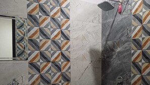 A bathroom with a sink, mirror, shower, and tiled walls. - The Hotel JRS (Rishikesh)