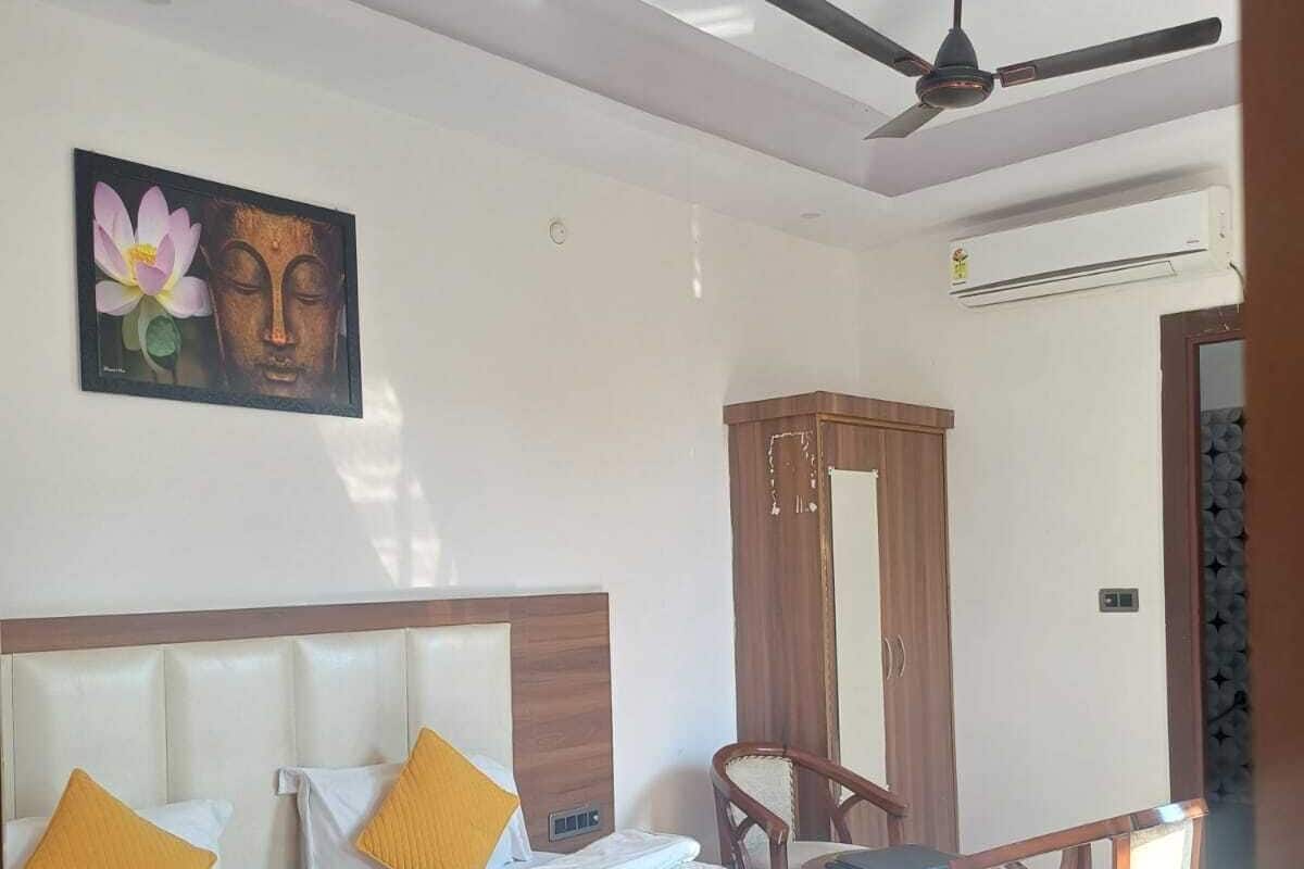 Una habitación de hotel con cama, escritorio, silla, ventilador de techo y aire acondicionado instalado en la pared.