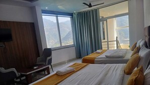A hotel room with two beds, a desk, a chair, a TV, and a large window with curtains. - The Hotel JRS (Rishikesh)