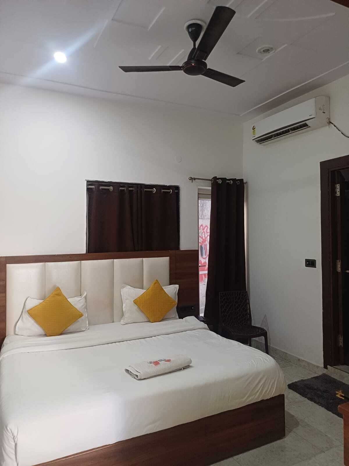 A hotel room with a bed, a ceiling fan, an air conditioning unit, and a window with curtains.